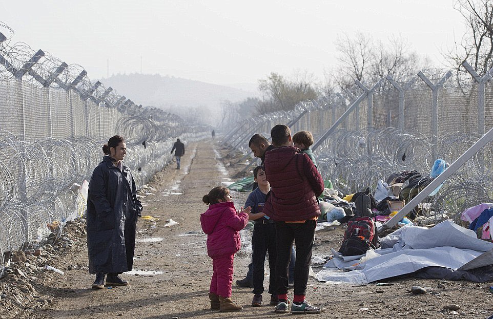 A family of refugees wait in the no-man's-land area at the border which is guarded by barbed wire fences. Macedonia has closed its border with Greece, causing a bottleneck among those travelling the Balkan route.jpg